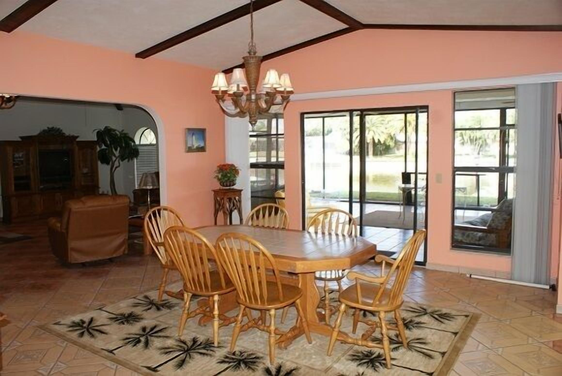 A dining area with a wooden table and chairs, a chandelier, and a view through large sliding glass doors.
