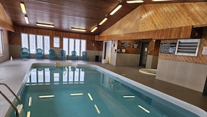 Une piscine intérieure dotée d’un plafond et de murs en bois, entourée de chaises bleues.