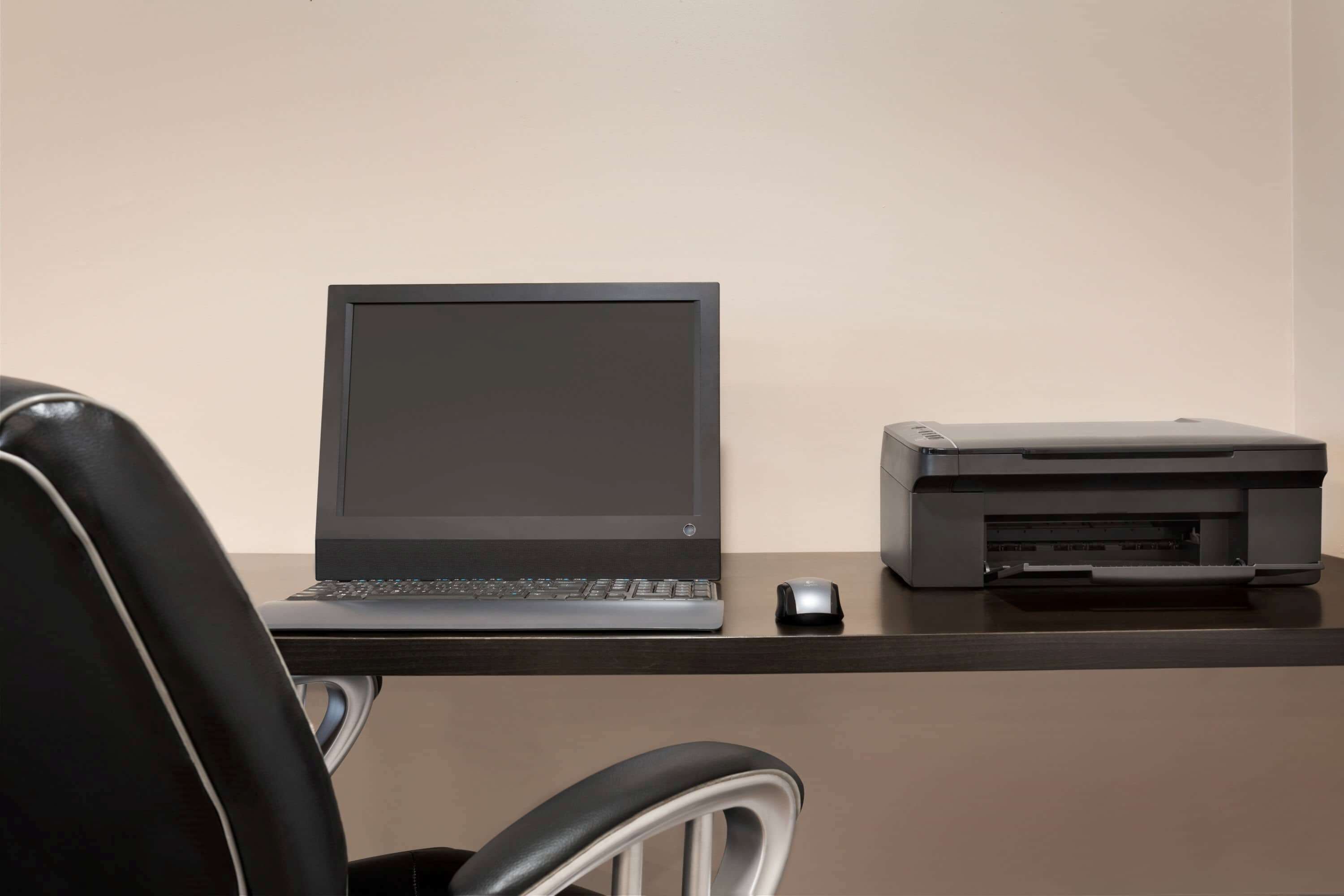 A desk with a laptop, a printer, and a mouse.