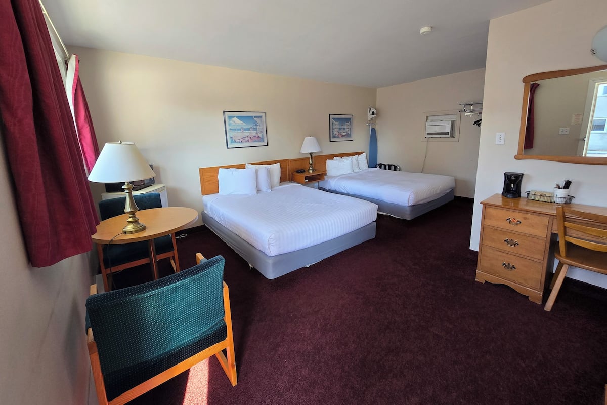 Een hotelkamer met twee bedden, een bureau, een stoel, een lamp, een koffiezetapparaat en een spiegel.