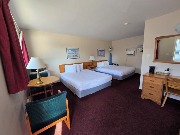 Une chambre d’hôtel avec deux lits, un bureau, une chaise, une lampe, une machine à café et un miroir.