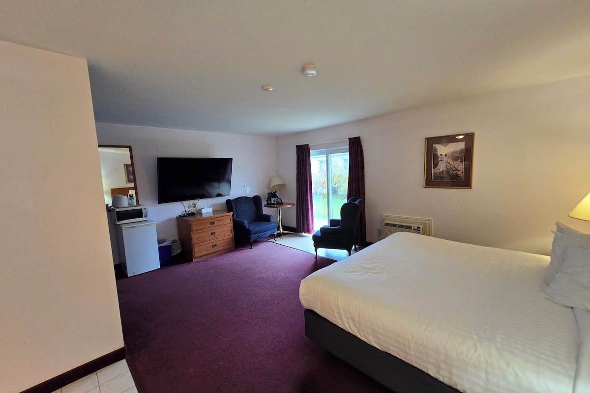 Een hotelkamer met een bed, een bureau met een computer, een stoel, een televisie en een raam met gordijnen.