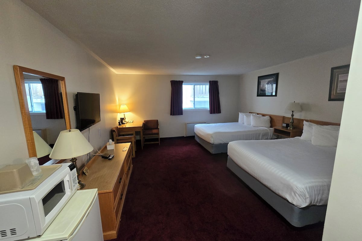 Een hotelkamer met twee bedden, een bureau met lamp, een magnetron, een televisie en een raam met gordijnen.