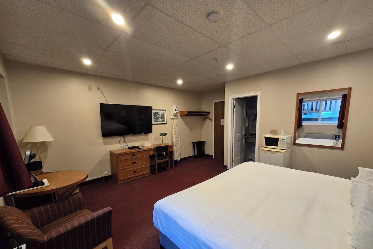 Een hotelkamer met een bed, een bureau met een televisie, een stoel, een kapstok en een klein raam.