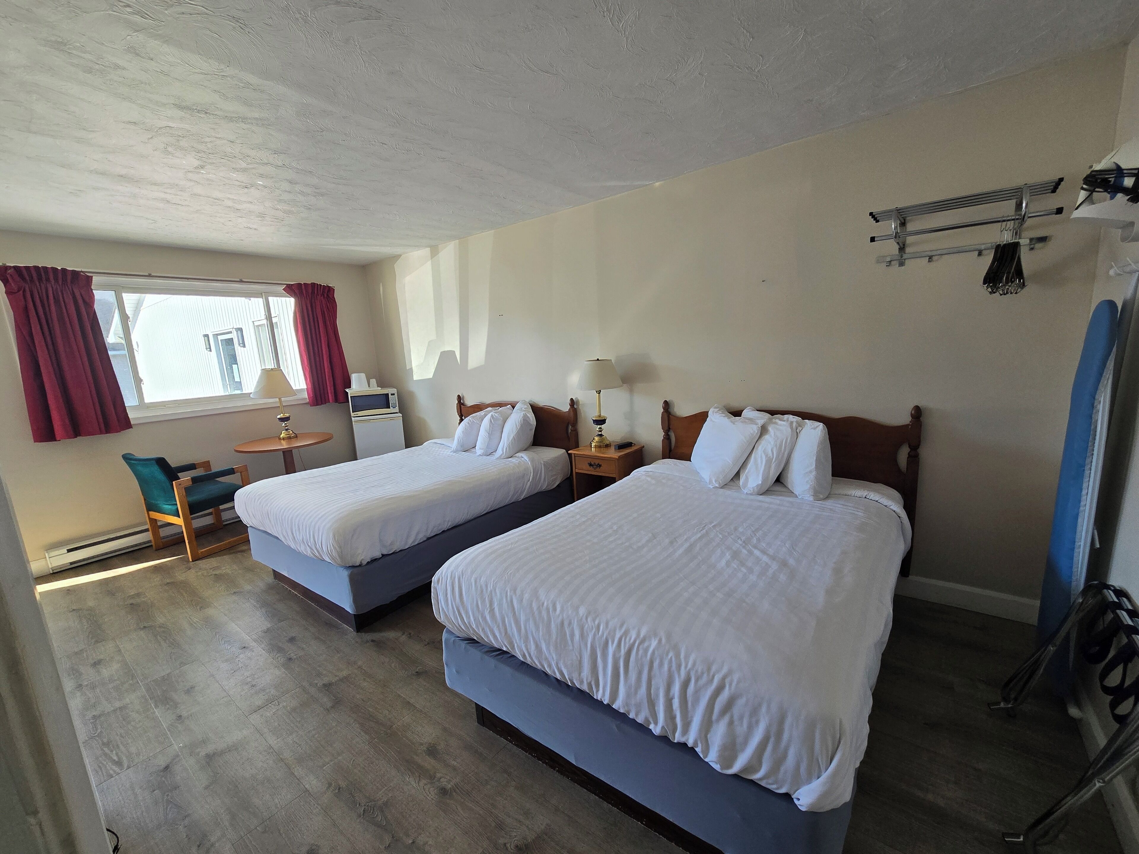 A hotel room with two beds, a desk with a chair, a microwave, and a small table with a lamp.
