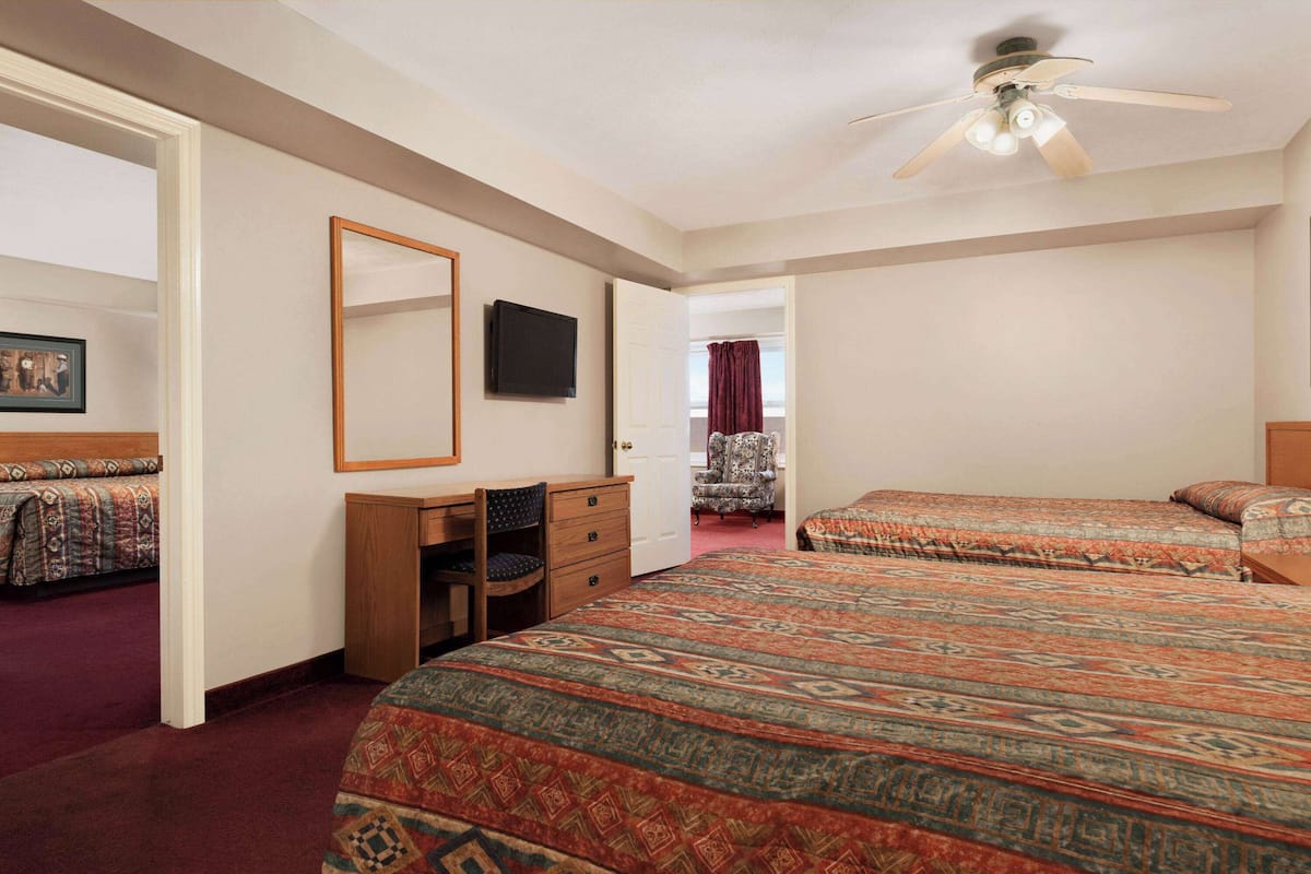 Een hotelkamer met twee bedden, een bureau, een stoel, een televisie en een plafondventilator.