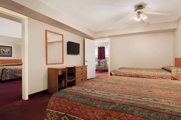 A hotel room with two beds, a desk, a chair, a television, and a ceiling fan.