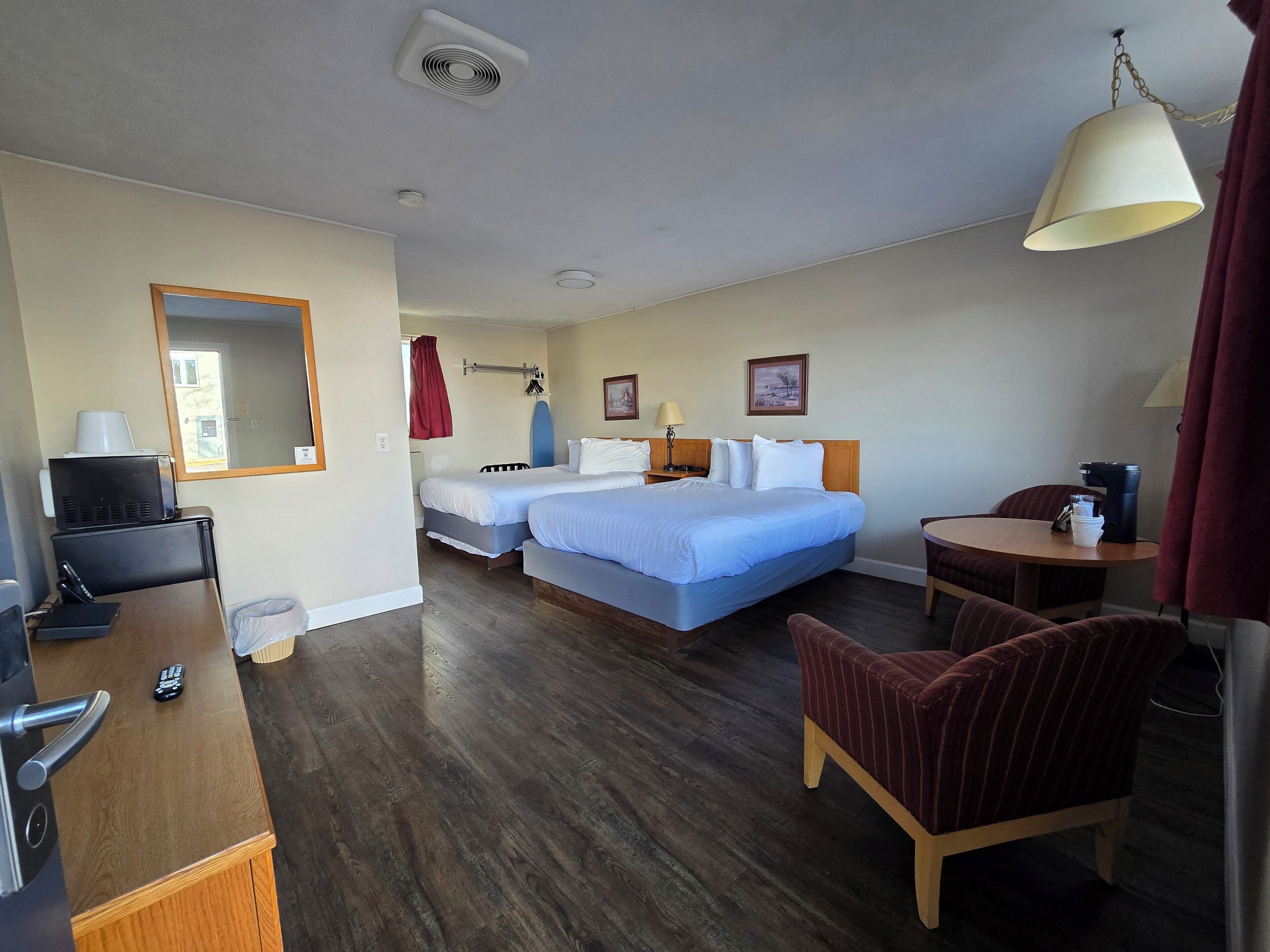 A hotel room with two beds, a desk with a computer, a chair, a lamp, and a coffee machine.