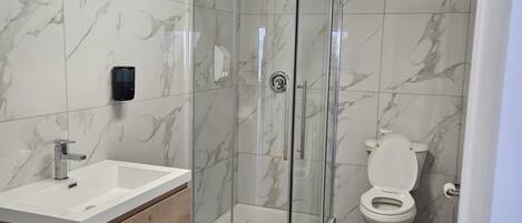 Un baño moderno con cabina de ducha de vidrio, tocador de madera y un inodoro.