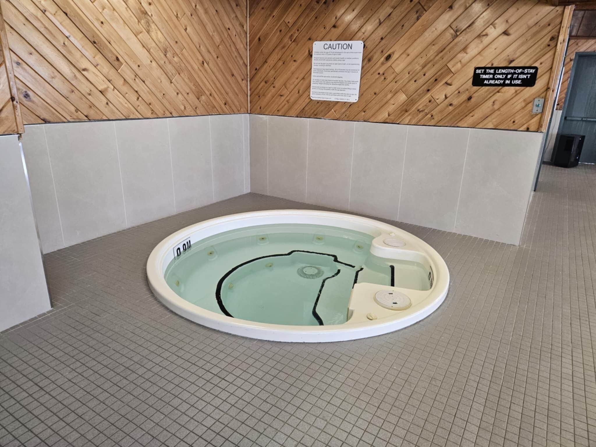 A small, circular hot tub with a wooden wall and tiled floor.