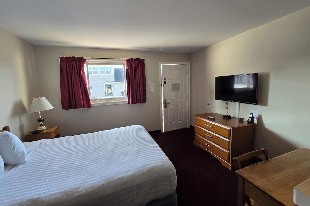 Een hotelkamer met een bed, bureau, dressoir, televisie en een raam met gordijnen.
