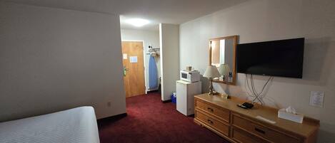 Een hotelkamer met een bed, een houten dressoir, een bureau met lamp, een magnetron, een televisie en een rode vloerbedekking.