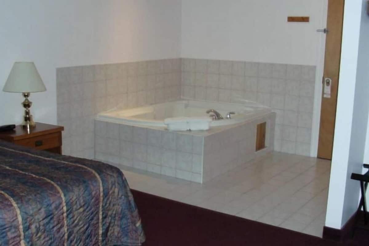 Een hotelkamer met een bed, een nachtkastje met een lamp en een groot bad.