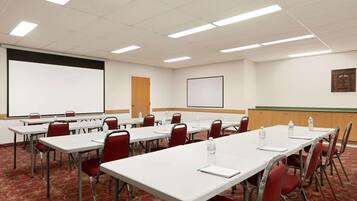Un salón de conferencias con mesas blancas, sillas rojas y una pantalla de proyector.