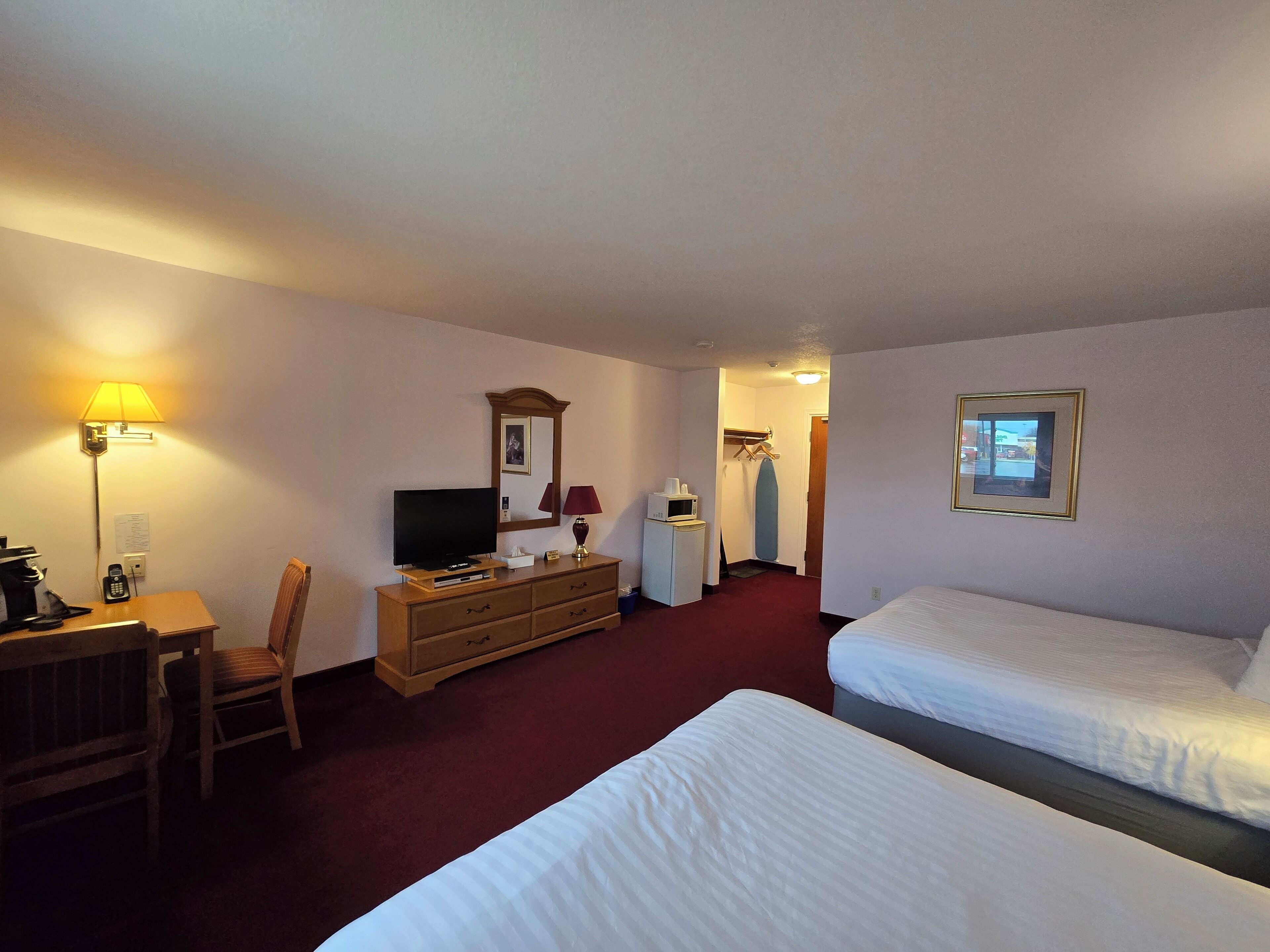 Habitación de hotel con dos camas, un escritorio con lámpara, cómoda, televisor y espejo.