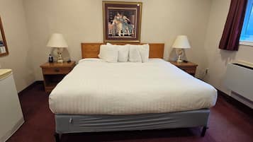 Quarto de hotel com uma cama grande, duas mesas de cabeceira com luminárias, um quadro na parede e uma janela com cortinas.