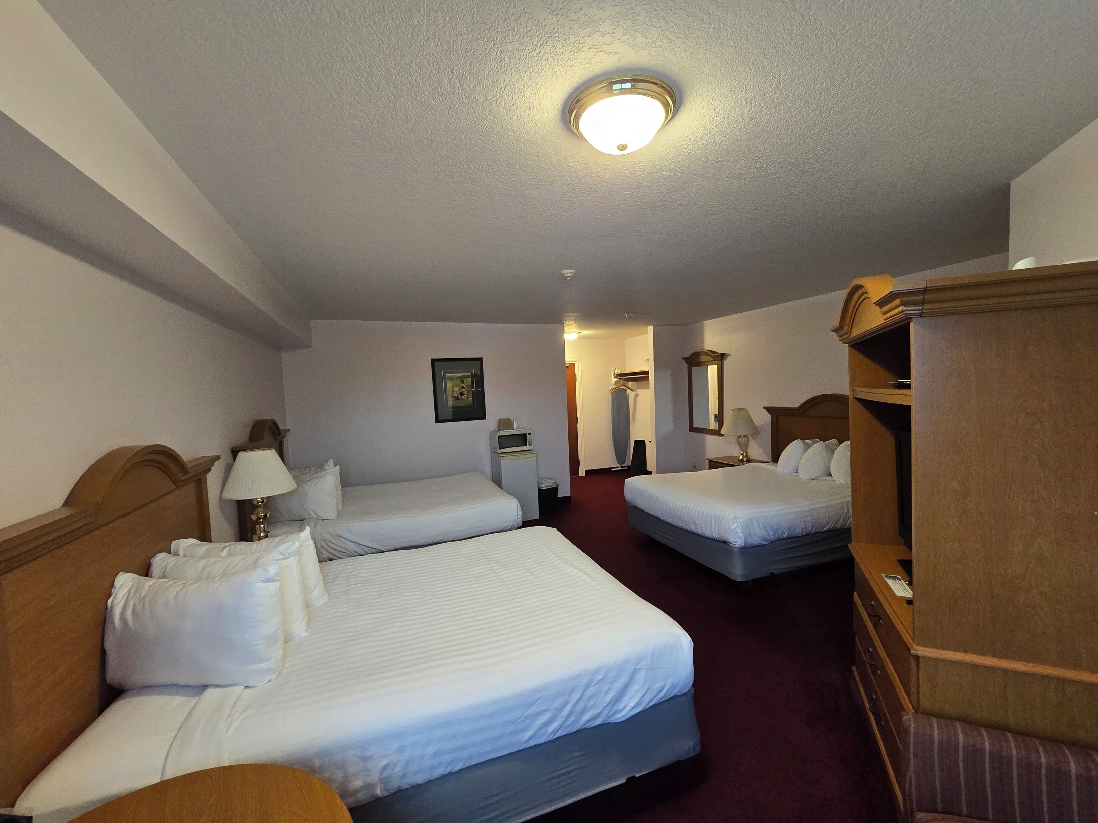 A hotel room with two single beds, a wooden wardrobe, a desk with a lamp, and a framed picture on the wall.