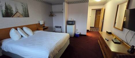 A hotel room with a bed, bedside table, TV, and a desk with a chair.