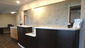 Un espace d ’accueil avec un comptoir de réception sombre, un comptoir blanc et un mur en briques.