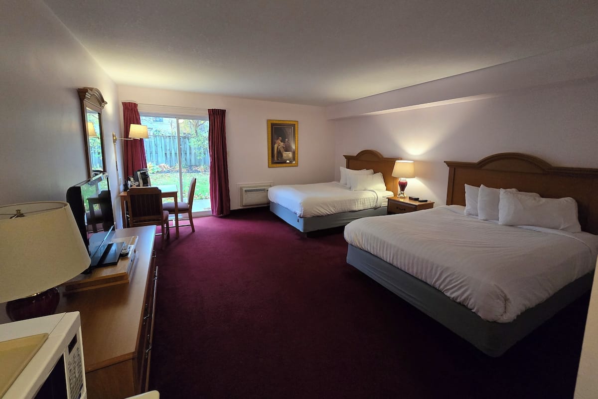 Een hotelkamer met twee bedden, een bureau met een computer, een stoel, een raam met gordijnen en een schilderij aan de muur.