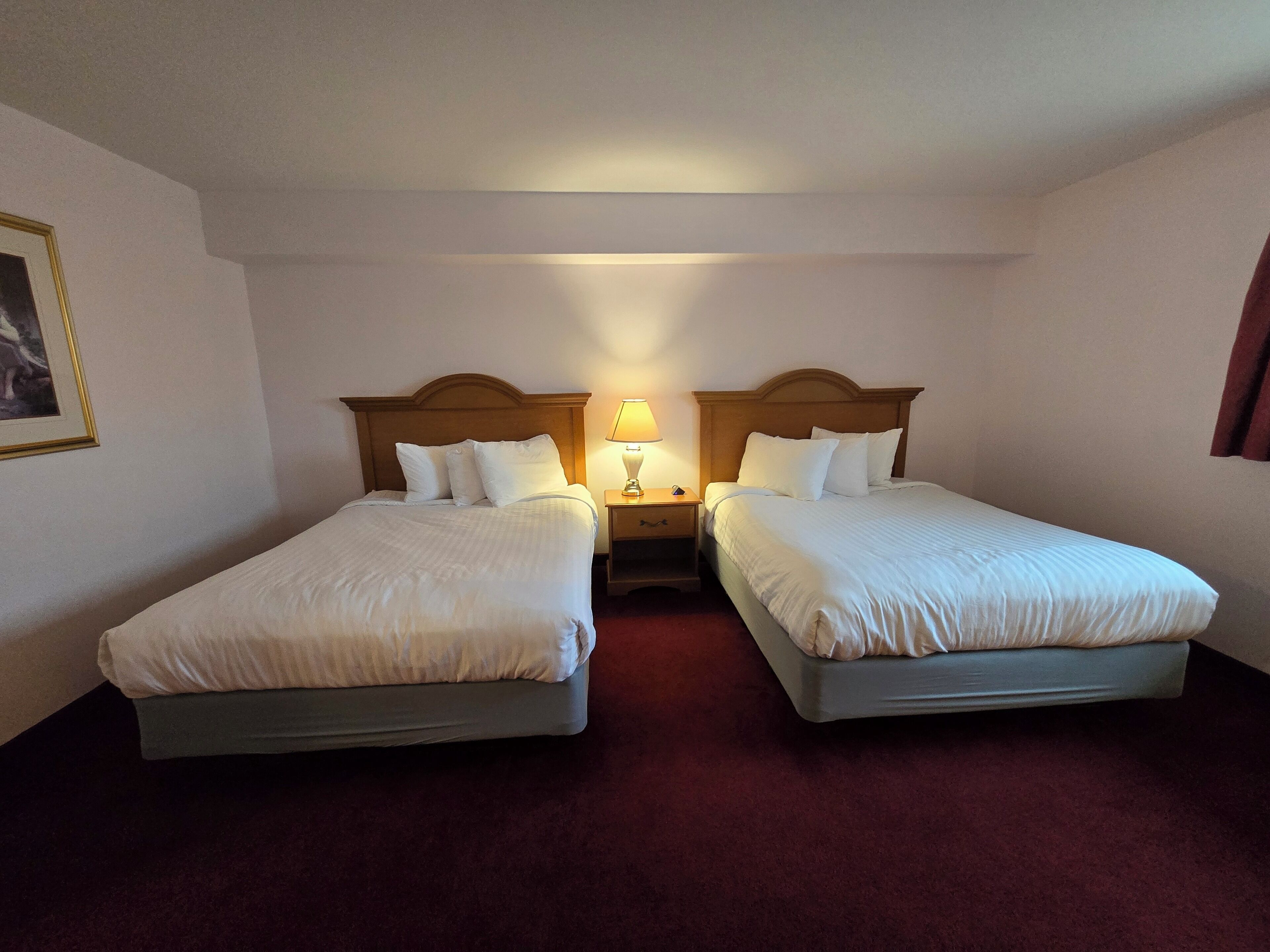 A hotel room with two beds, a nightstand with a lamp, and a framed picture on the wall.