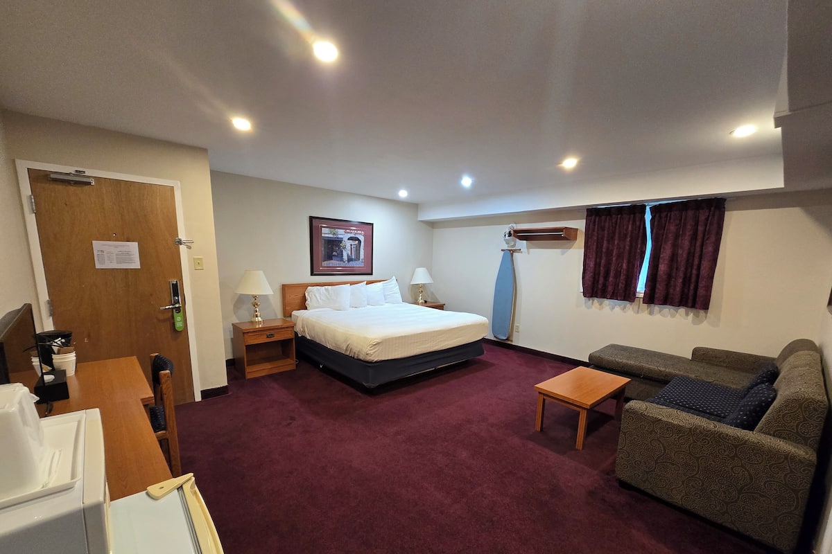 Een hotelkamer met een bed, een bank, een kleine tafel, een bureau, een lamp, een deur en een raam met gordijnen.
