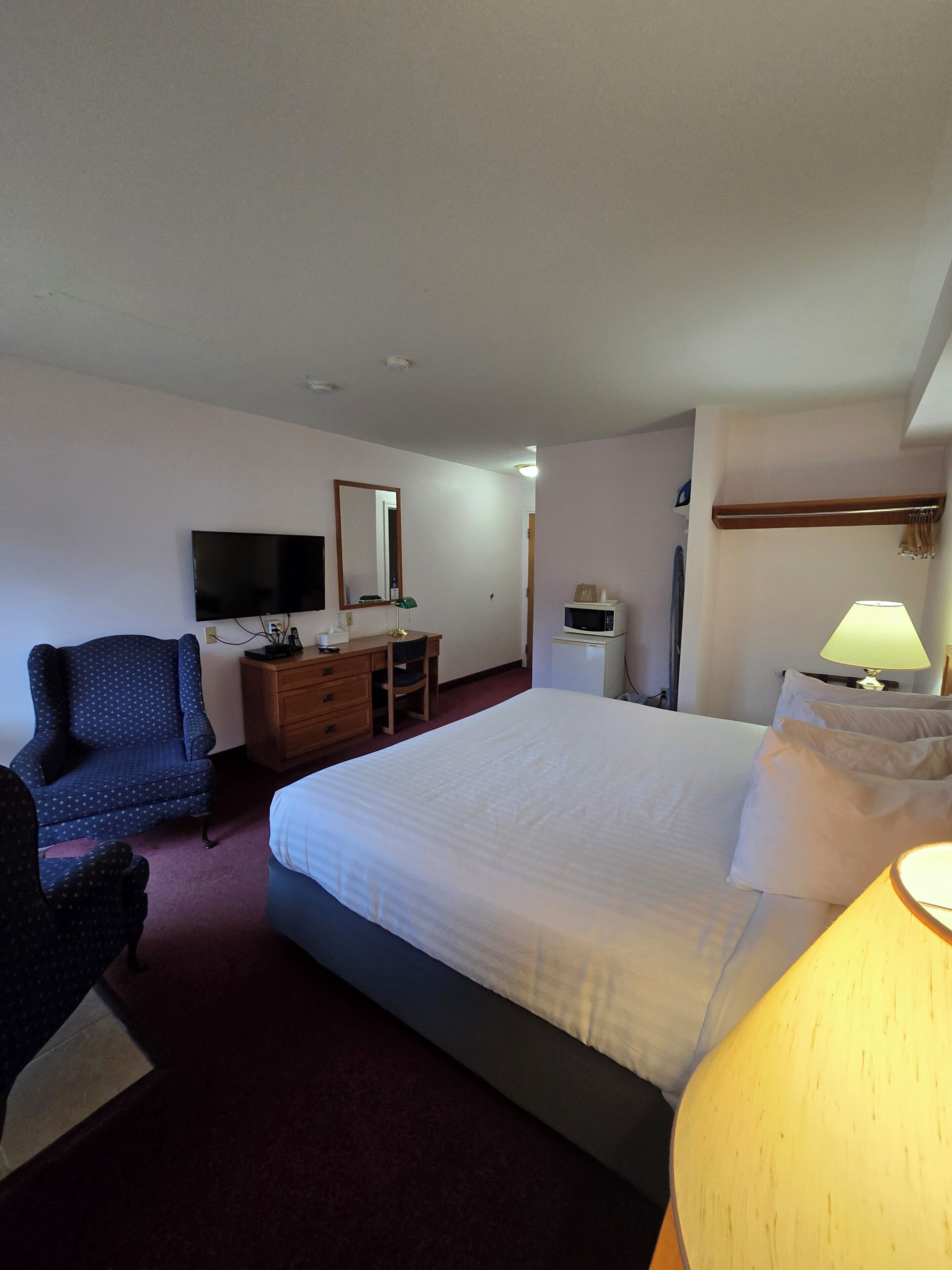 Een hotelkamer met een bed, een bureau, een stoel, een televisie, een magnetron en een lamp.