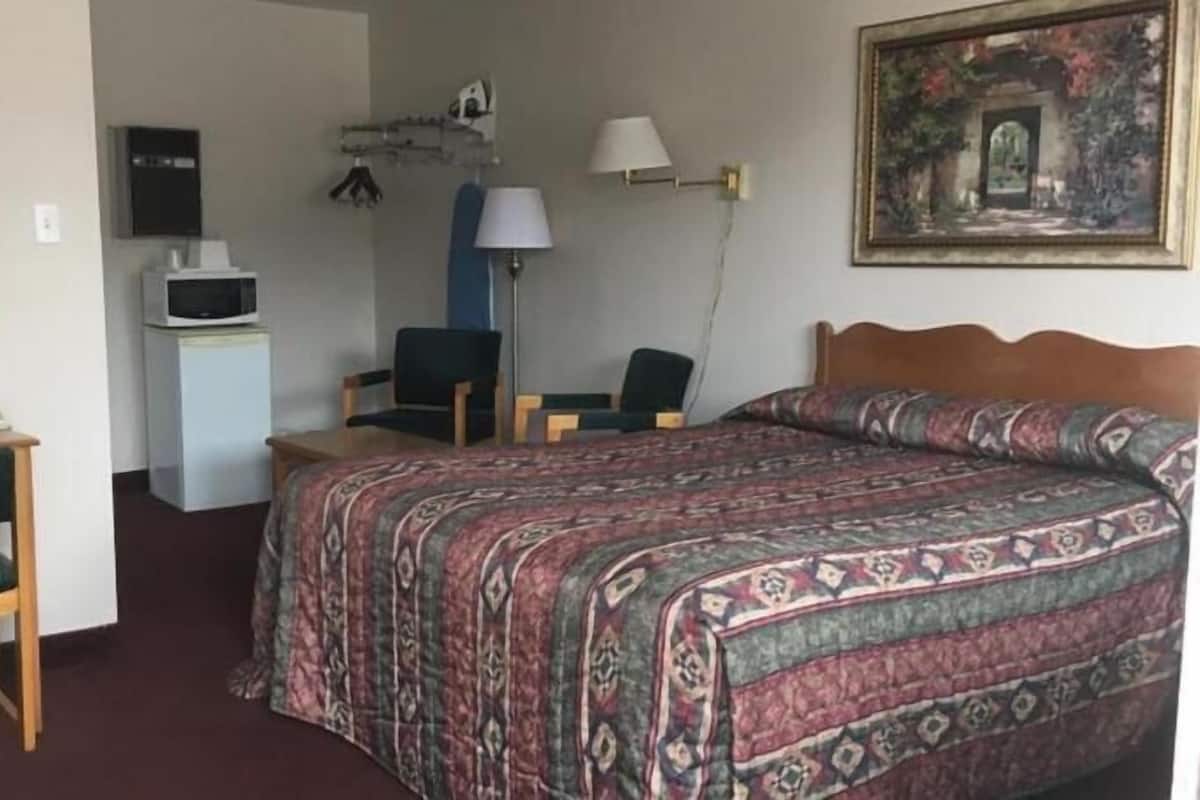 Een hotelkamer met een bed, een bureau met telefoon, een stoel, een televisie en een schilderij aan de muur.
