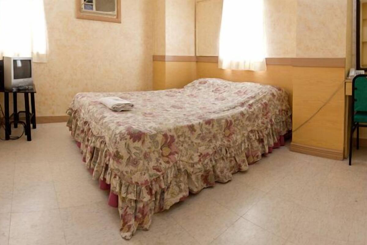 Una habitación con una cama individual, un escritorio pequeño, una silla y un televisor.