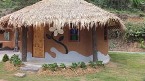 Una cabaña con techo de paja, una puerta y una ventana, rodeada de follaje.