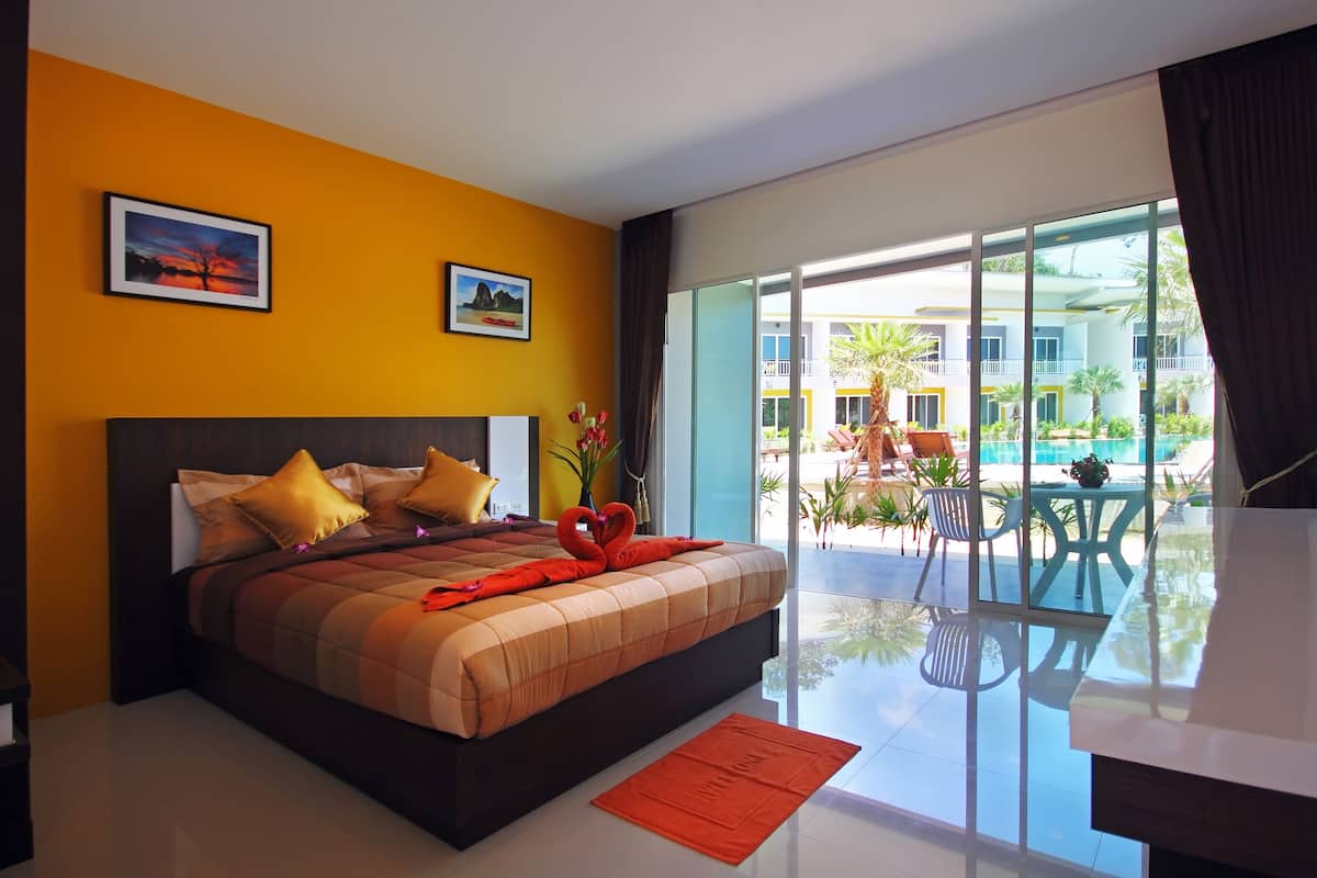 A modern hotel room with a large bed, a view of the pool, and a balcony with outdoor furniture.