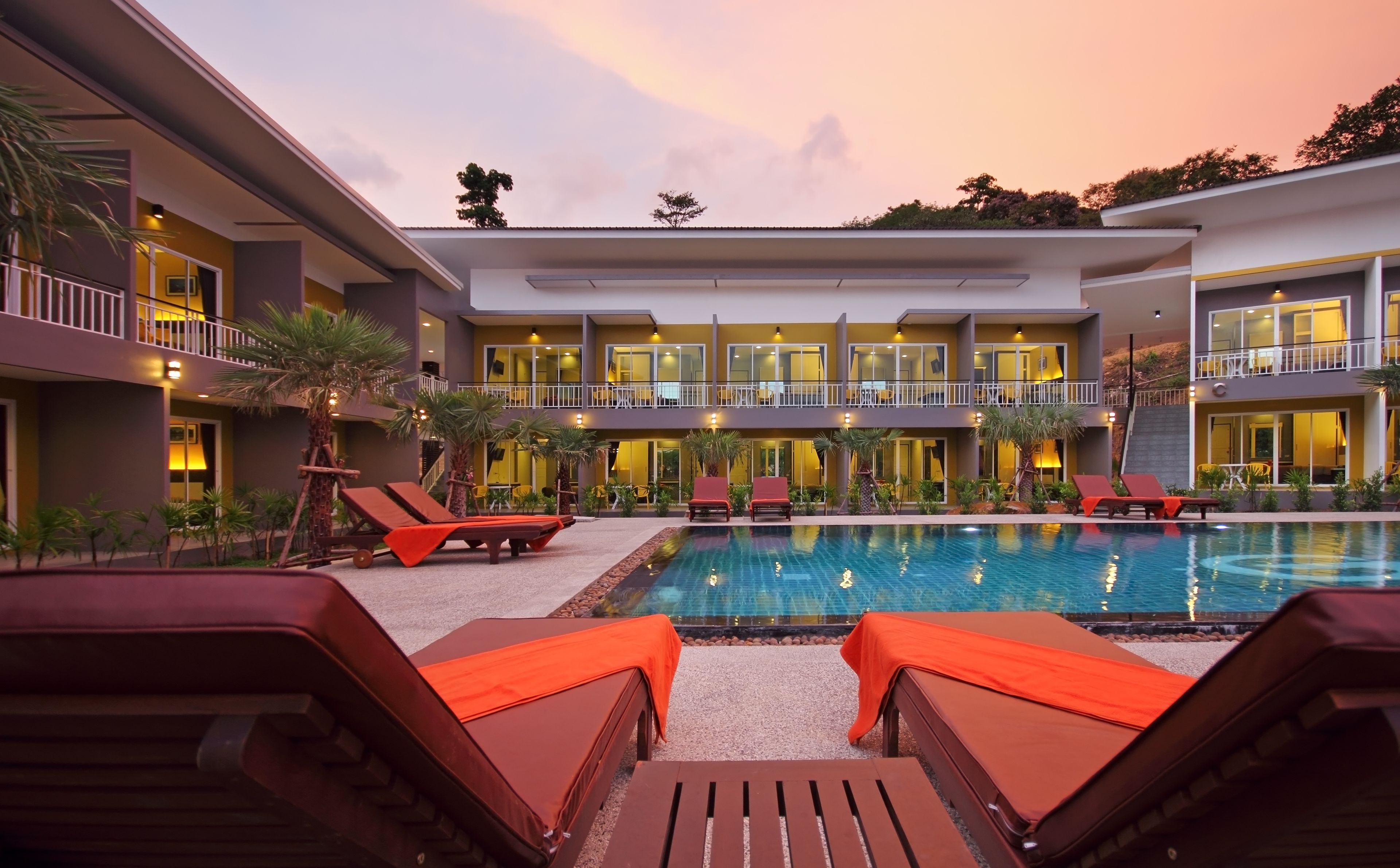 A modern hotel with a swimming pool, sun loungers, and a covered outdoor area.