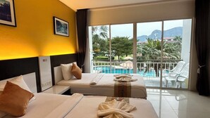 Habitación de hotel con dos camas, vista a una piscina y un balcón con sillas blancas.