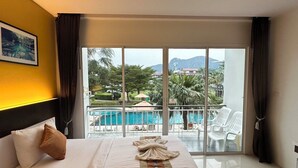 A hotel room with a bed, a view of a pool and outdoor seating, and a painting on the wall. - Gypsy Sea View Resort (Ko Phi Phi)
