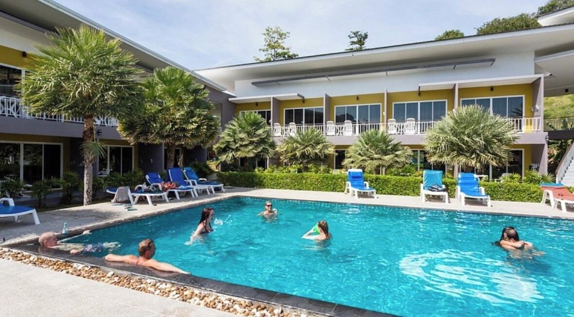 A swimming pool with lounge chairs and palm trees, surrounded by a building with balconies.