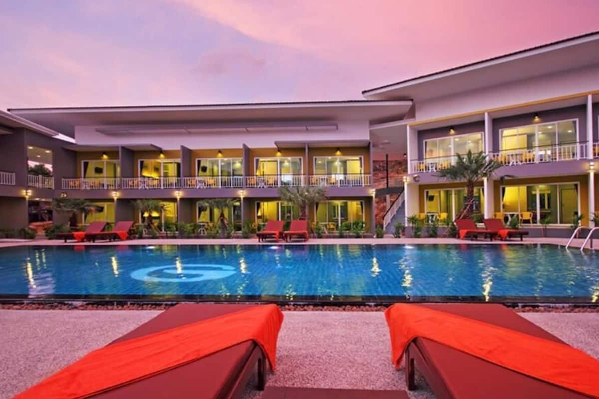 A hotel with a pool, multiple balconies, and red lounge chairs.