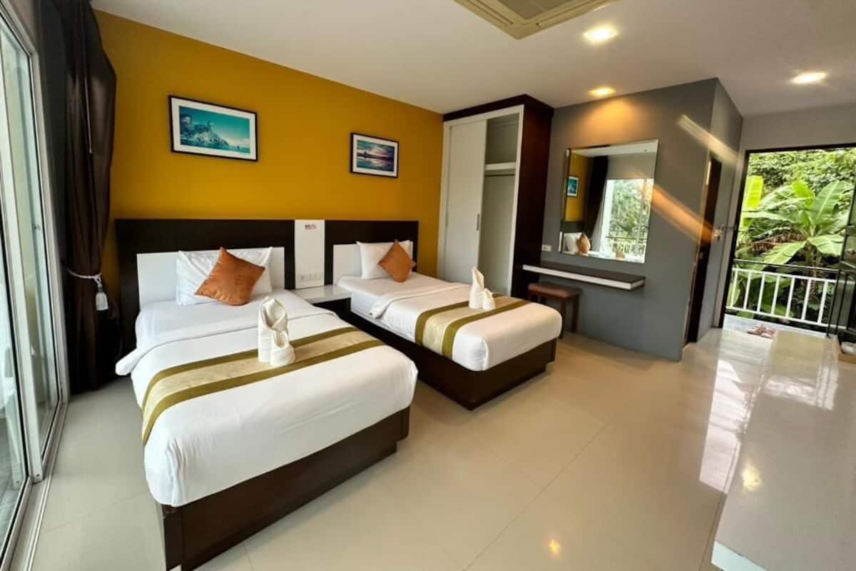 A hotel room with two beds, a small desk, a mirror, and a view of greenery outside.