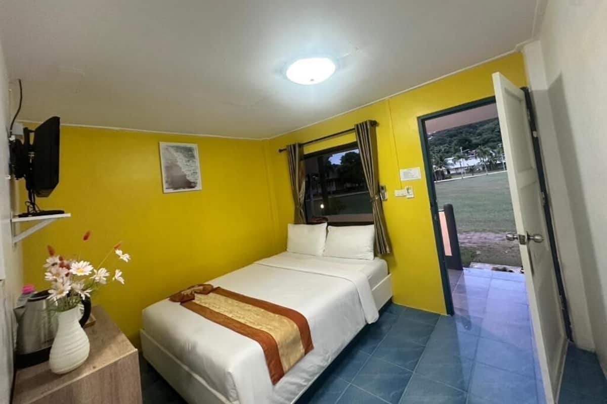 A single bed in a room with yellow walls, a window with curtains, and a door leading outside.