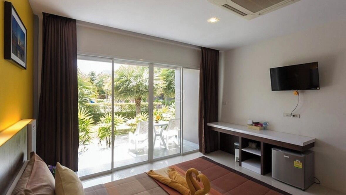Una habitación con puerta corrediza de vidrio a un patio, televisor de pantalla plana en la pared, una kitchenette pequeña y un sofá.