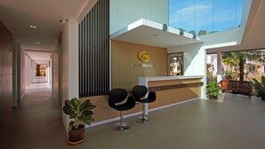 A reception area with a wooden reception desk, two black chairs, and a large window offering a view of the outdoors. - Gypsy Sea View Resort (Ko Phi Phi)
