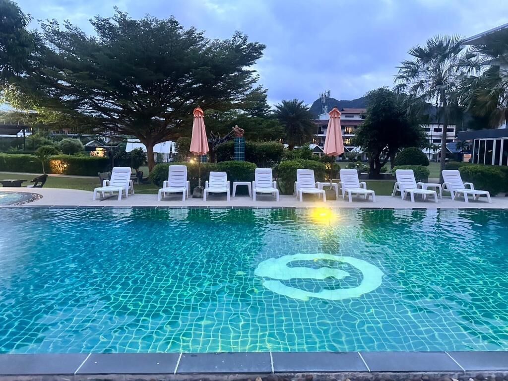 A swimming pool with lounge chairs and umbrellas, surrounded by trees and buildings.