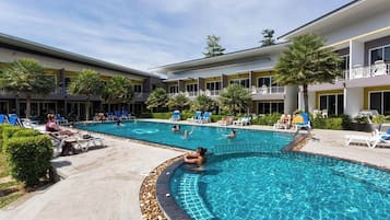 A hotel pool area with multiple pools, lounge chairs, and palm trees.