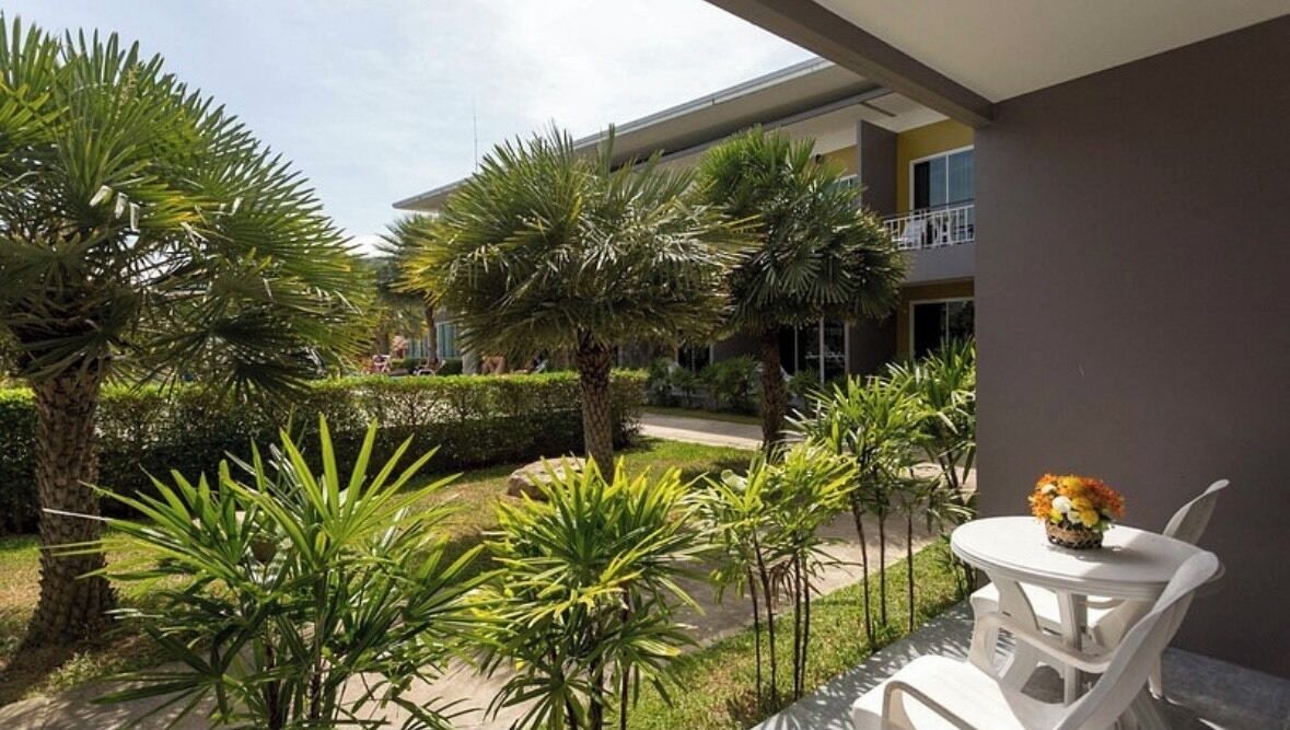 Een hotel binnenplaats met palmbomen, een witte tafel met een bloevas en een gebouw met balkons.