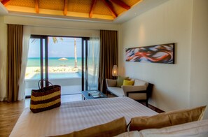 A hotel room with a bed, a desk, a chair, a large window with a view of the beach, and a painting on the wall. - Kandaya Resort (Daanbantayan)