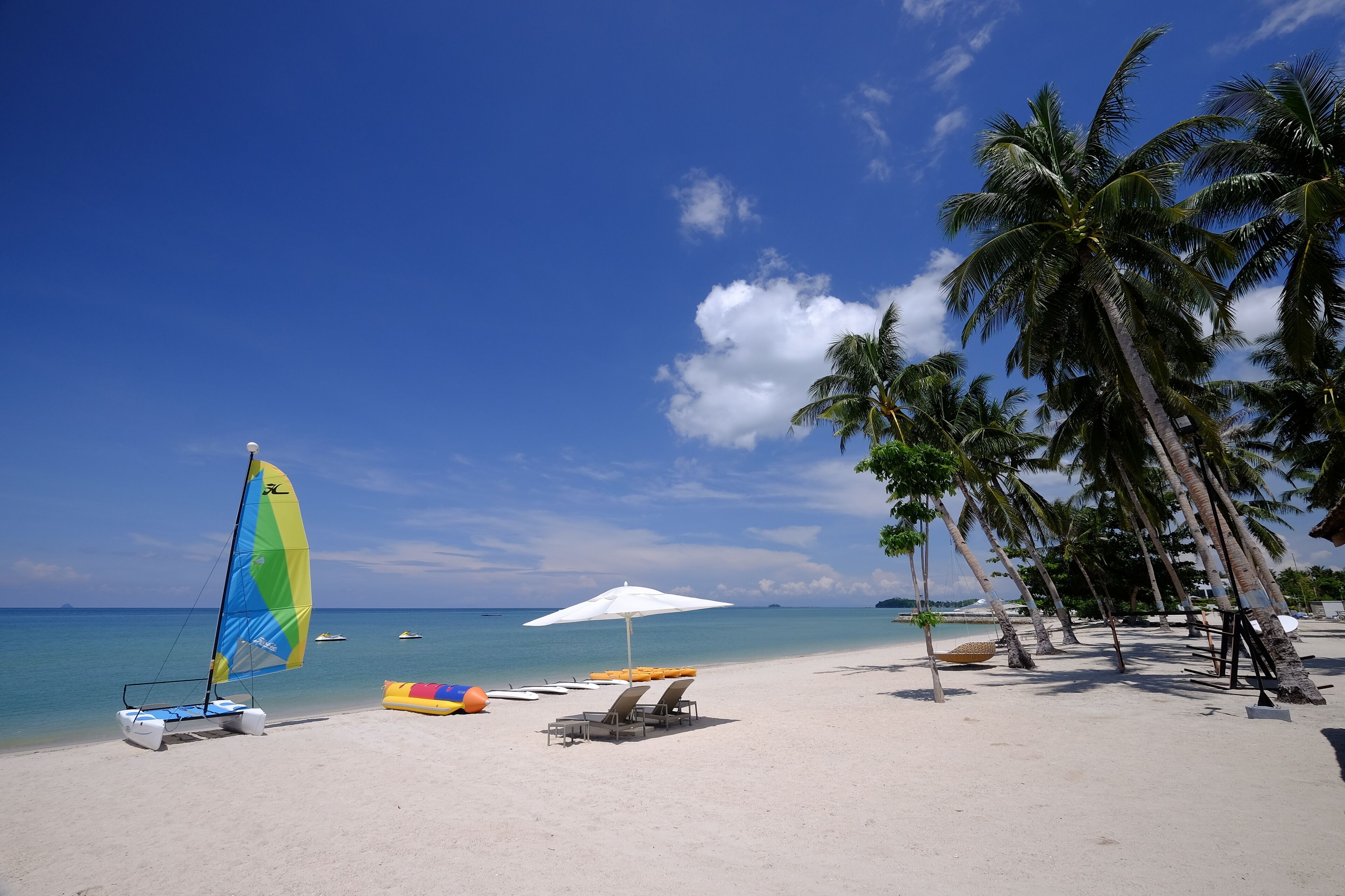 Een strand met een zeilboot, ligbedden en parasols.