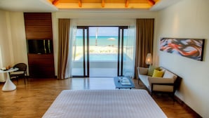 Een hotelkamer met een groot bed, een televisie, een bank, een bijzettafeltje en uitzicht op het strand.
