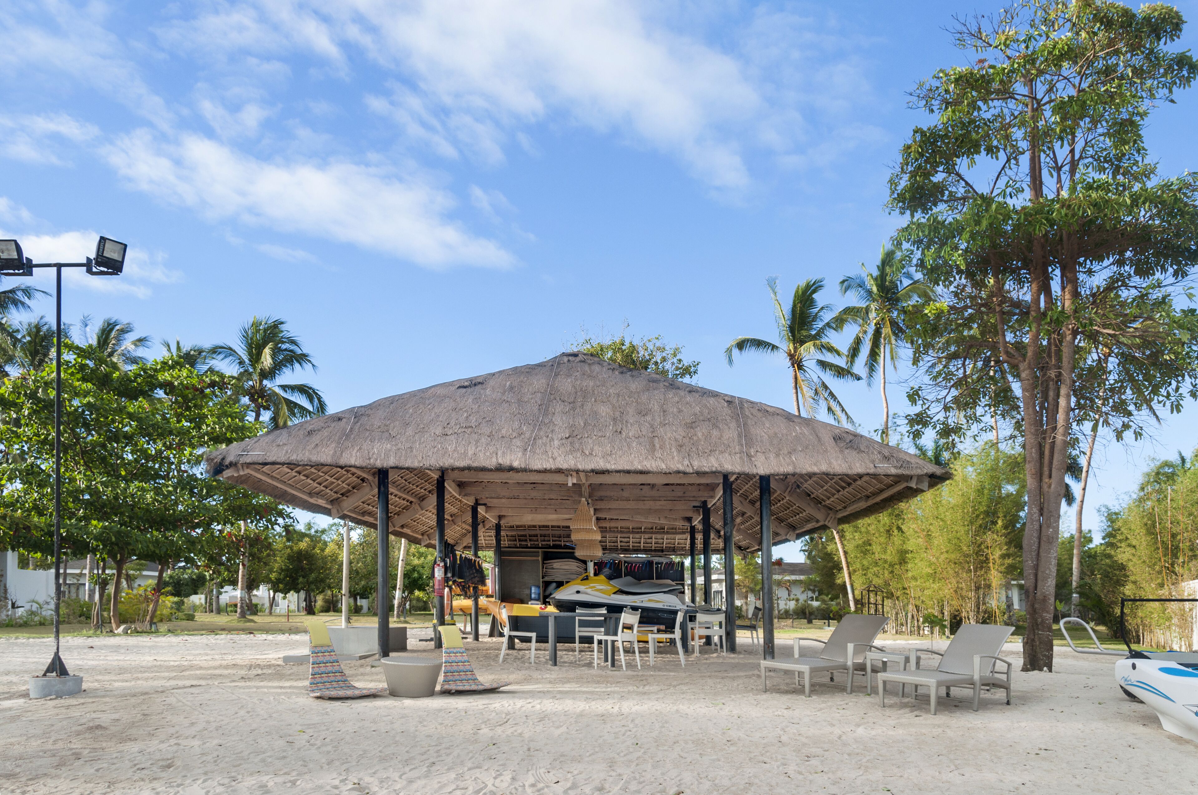 Un pavillon situé au bord de la plage, doté d’un toit de chaume, d’un espace salon et d’un jet ski.