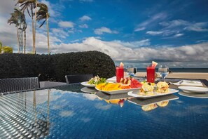 A table set for a meal with tropical fruit and beverages, overlooking a beach and palm trees. - Kandaya Resort (Daanbantayan)