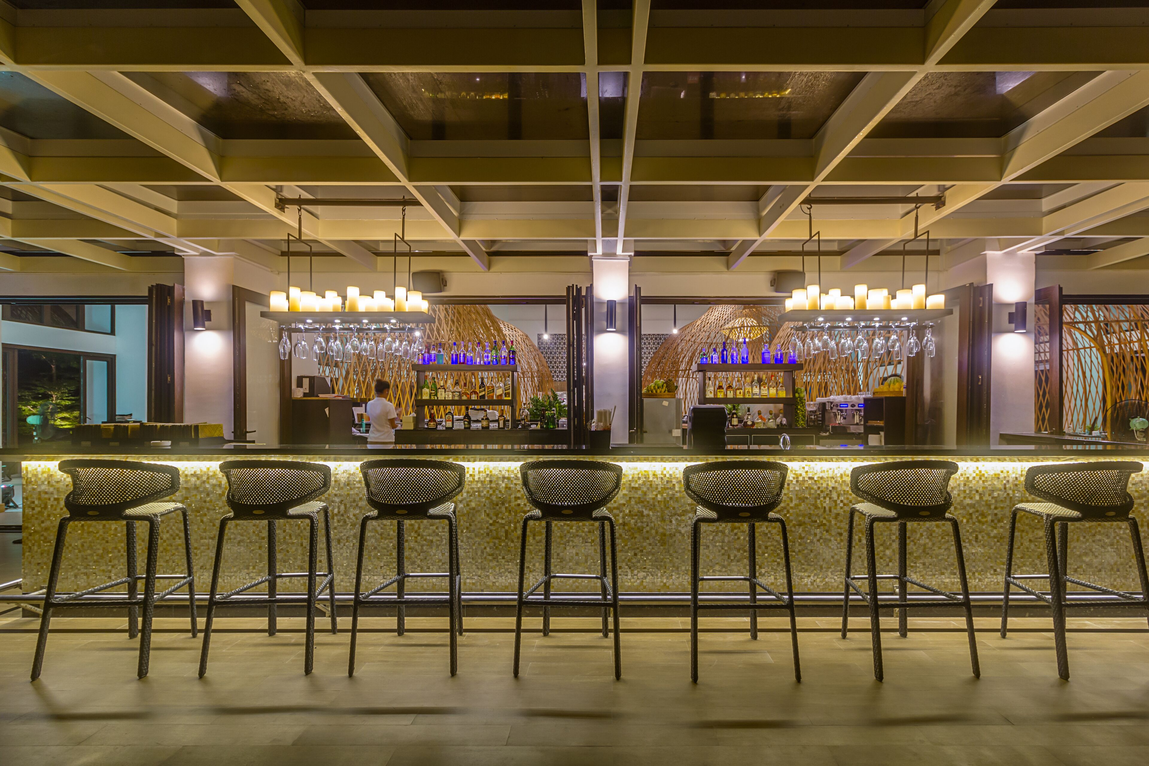 A bar area with a counter, bar stools, and a display of bottles and glasses.