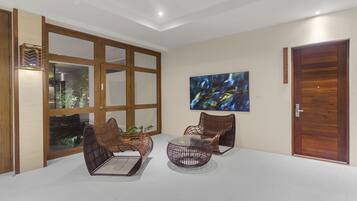 A spacious room with a large window, two wicker chairs, a round table, and a wooden door.